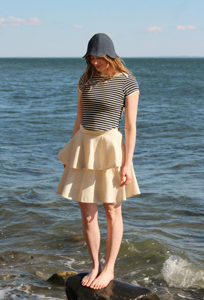 Woman standing on a rock by the ocean wearing a striped shirt and skirt.